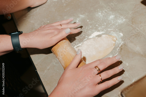 Hands rolling out fresh dough with a wooden rolling pin.