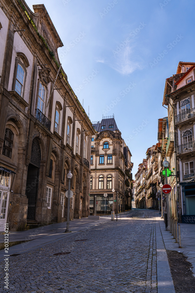 Fototapeta premium Historic narrow street in Porto Portugal lined with traditional tiled buildings and balconies. Sunny day with clear blue sky creating depth perspective and authentic European city atmosphere.