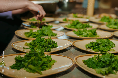 Chef arranging green lettuce on many plates for a banquet.
