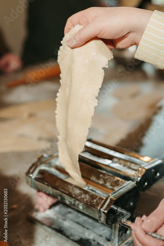 Person feeding a thin sheet of dough into a pasta machine.