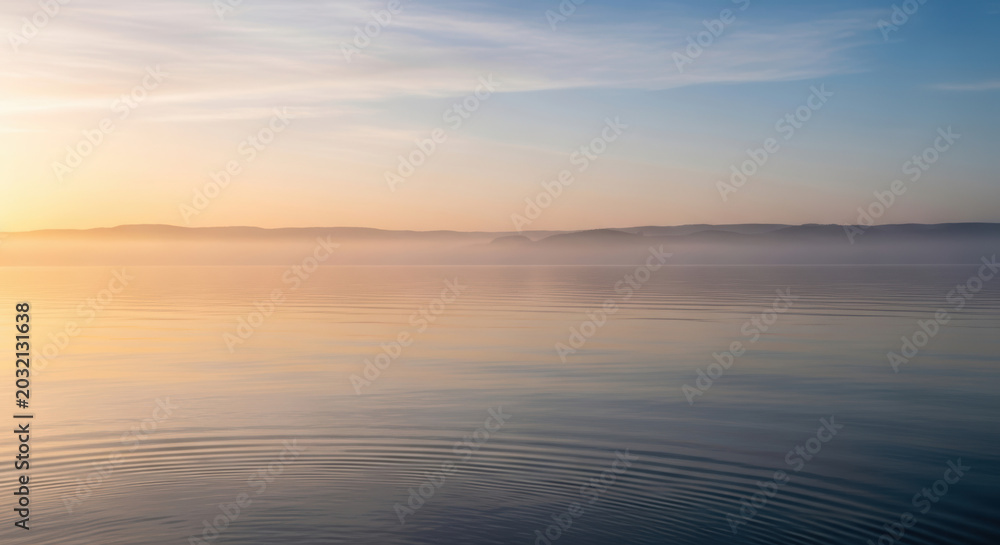 Obraz premium Sunset over calm ocean waves with golden sky reflection