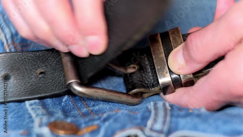 Person fastening leather strap carefully. Focused shot capturing fingers threading leather strap through metal buckle and keeper