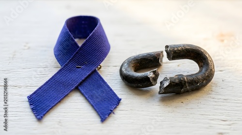 Purple awareness ribbon next to a broken metal chain link on a white wooden surface, symbol of support and advocacy for health awareness and overcoming challenges