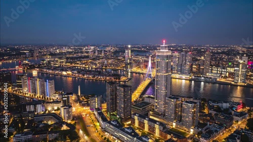 Aerial timelapse of a modern metropolis skyline at night with an illuminated bridge and river traffic