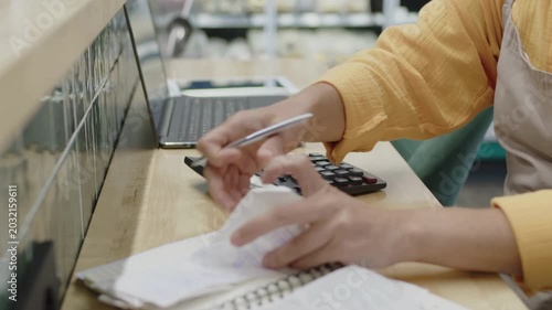 Small business owner in an apron calculating expenses with a calculator and receipts