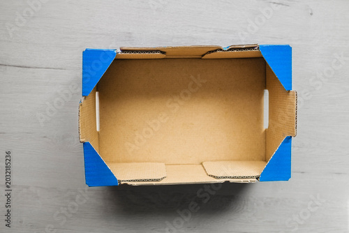 Εκτύπωση καμβά Empty cardboard box with blue protective corner guards on light gray wooden surf