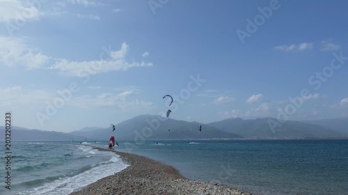 Wide angle kitesurfers racing across waves on Greek island beach