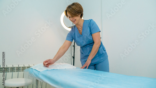 Bild auf Leinwand cosmetologist unfolds disposable paper on a treatment bed, preparing a clean surface in a professional beauty clinic