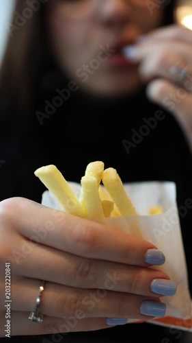 Vertical screen female eating french fries in stylish fast food spot realistic social dining atmosphere with modern cafe interior and urban youth lifestyle