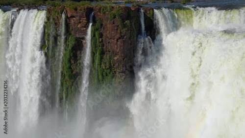 Majestic waterfalls of Iguazu cascading over a vertical cliff with vibrant green plants growing on wet rocks, a breathtaking natural wonder located on the border of Argentina and Brazil