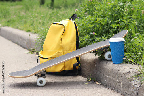 Foto Skateboard, yellow backpack and coffee on the side of the road