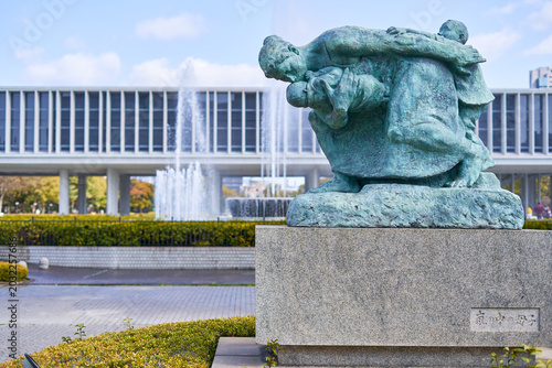 Bild auf Leinwand A bronze statue with green patina depicting a mother carrying two children, positioned on a granite pedestal with Japanese inscription reading Mother and Child in the Storm