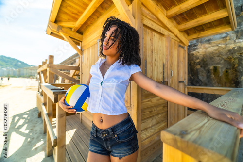 Woman holding volleyball relaxing by wooden beach hut