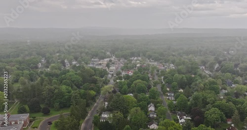 Red Hook, NY, USA - 05-20-2026  Aerial hyperlapse video of rainstorm over a small town nestled within a vast expanse of lush green forest under a partly cloudy sky.
