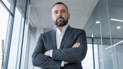 Confident Mature Businessman Standing with Crossed Arms in Modern Office