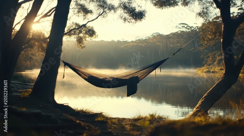 A tranquil hammock strung between trees overlooking a serene lake at sunrise, perfect for peaceful relaxation and enjoying nature's beauty.