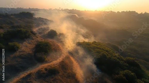 Forest fire smoke blanketing a mountainous hiking trail during soft evening light, viewed from above.