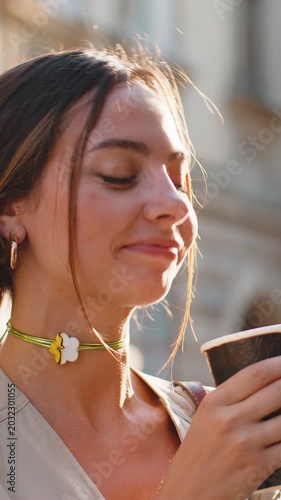 Happy pretty young woman enjoying morning coffee hot drink and smiling outdoors. Relaxing, taking a break. Lady walking in urban city sunshine street, drinking coffee to go. Town lifestyles outside