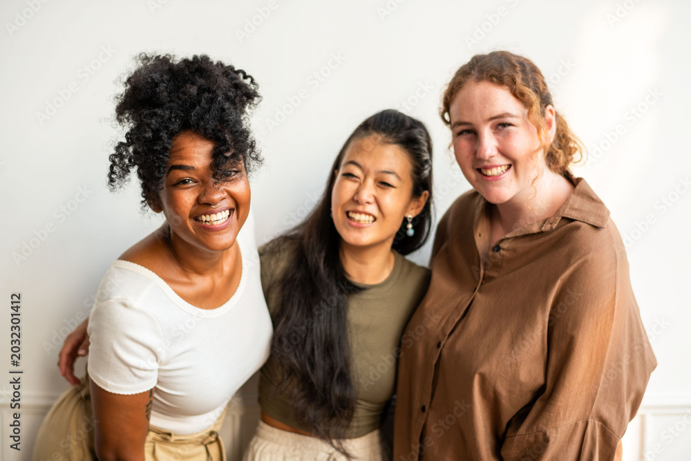 Fototapeta premium Three smiling women of diverse ethnicities posing together indoors