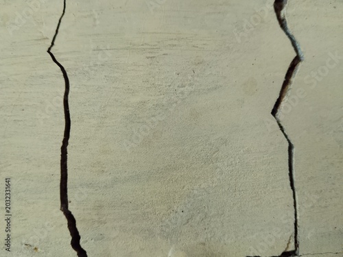 Cracked old wall texture with deep vertical fractures on weathered beige concrete surface background