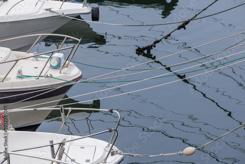Foto High-angle view of small fiberglass recreational boats docked side by side in calm water with multiple mooring lines stretching across dark rippling surface, creating abstract wavering reflections
