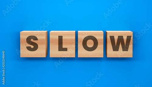 Konstfotografi Wooden Blocks Spell Slow: Four wooden blocks arranged on a vibrant blue surface spell out the word SLOW, symbolizing a deliberate pace or a period of inactivity