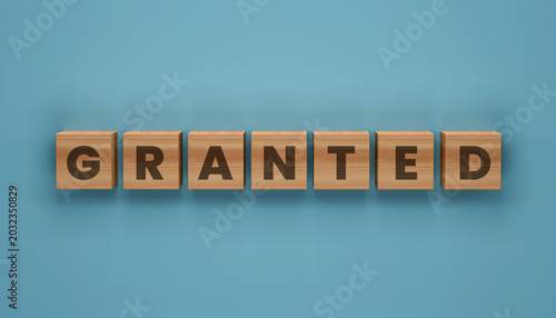 Obraz na plátne Grant Word Blocks: Seven wooden blocks, each displaying a letter from the word GRANTED, are arranged horizontally on a solid blue background, symbolizing approval and fulfillment