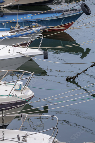 Foto Portrait view of layered boat bows quietly resting in a marina with crisscrossing mooring lines stretching over its calm, reflective water