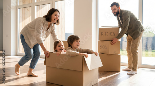 Happy family moves into bright new house while children play inside cardboard box parents carry packing boxes celebrating relocation fresh start home ownership joyful domestic lifestyle