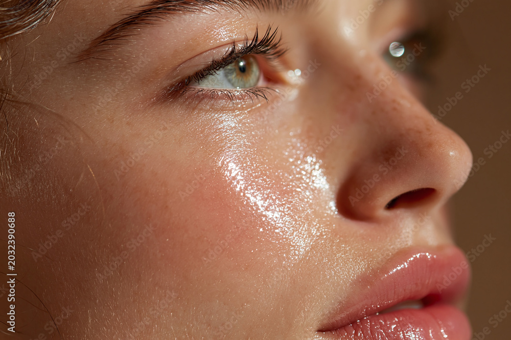 Naklejka premium Young woman close up skin glossy finish bright reflection on cheek and lips with natural freckle texture and soft light emotional gaze