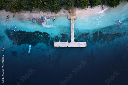 Aerial view of a small harbor and jetty on the coast of Morotai Island in North Maluku, Indonesia, with traditional fishing boats in clear tropical water.