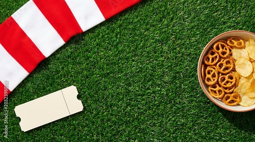 Flat lay top view of generic soccer fan scarf and ticket on green artificial grass