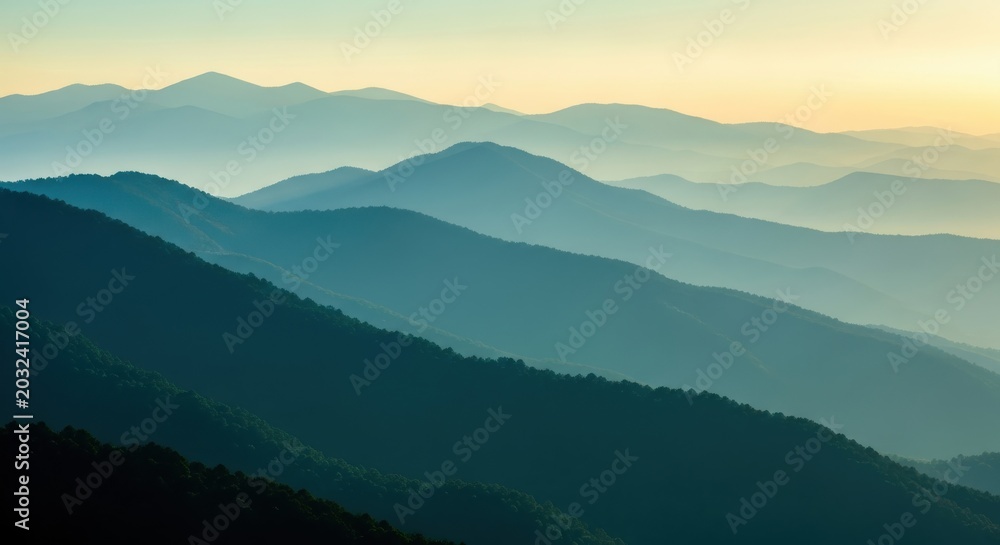 Naklejka premium Majestic Layered Blue Mountain Ridges at Sunrise with Misty Atmosphere and Golden Sky