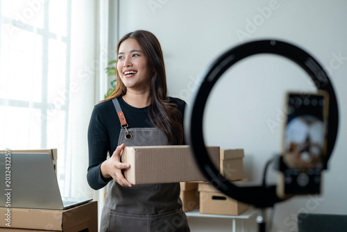 Young Woman Holding Package in Home Office Setting with Camera Setup