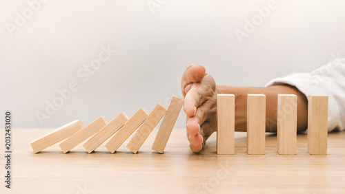 Hand stopping falling wooden domino blocks chain reaction concept for risk management crisis intervention protection insurance prevention strategy stabilization solution mitigation problem solving