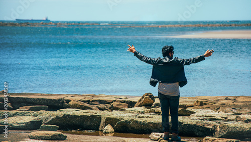 Foto Man standing on the rocky shore with his arms outstretched looking out at the ocean