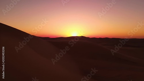 Desert dunes under a brilliant orange sunset with a lens flare