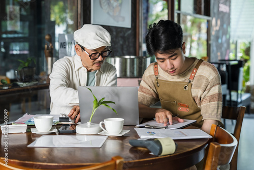 Asian father mentors teenage son through cafe paperwork, laptop inventory check, chart review, receipt control, daily lesson at family restaurant table, preparing successor for small business duty.