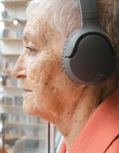 Senior woman profile wearing headphones listening to music, elderly mature female looking out window side view