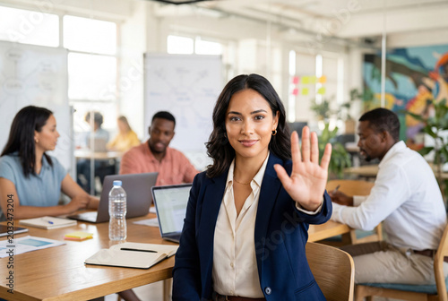 Confident businesswoman sitting at a desk holding her hand up in a stop gesture in a busy office