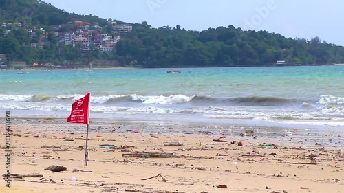 Red warning flag above polluted tropical beach with dangerous ocean debris Thailand.