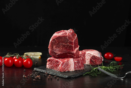 фотографія Raw Thick Cut Beef Steaks on Slate Board with Fresh Herbs and Vegetables for Gou