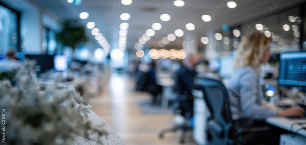 Fototapeta premium Modern Open-Plan Office Environment with Blurred Figures Working at Desks Under Bright Lights