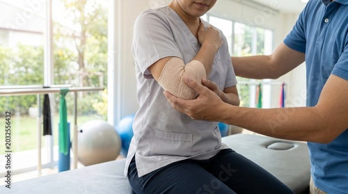 Physical therapist applying elastic bandage to woman elbow in clinic