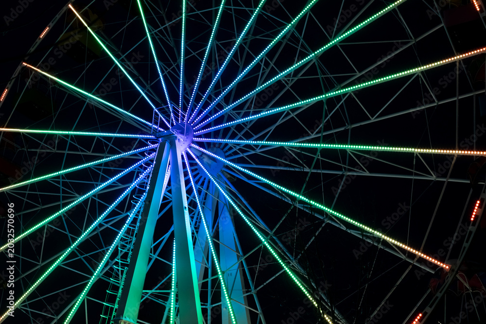 Fototapeta premium Nighttime Ferris wheel illuminated by colorful LED rings, wheel not moving