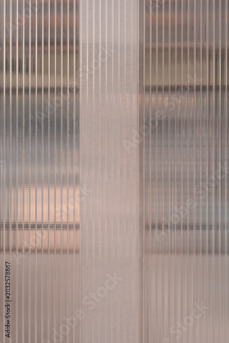 A full frame shot displays semi transparent ribbed glass panels separated by a vertical frosted dividing stripe with a soft brown abstract background.