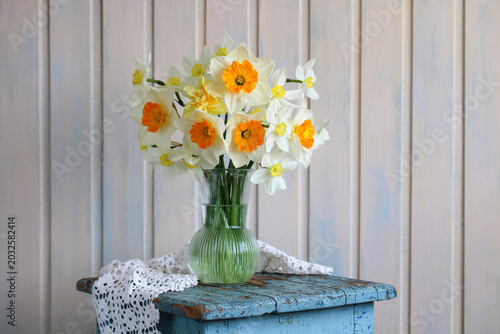 Bouquet of garden daffodils in a glass vase and white lace on a rough blue stool, rural still life
