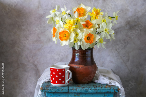 spring bouquet of garden daffodils of various varieties in an earthenware jug and a red mug with polka dots. Still life with yellow flowers.