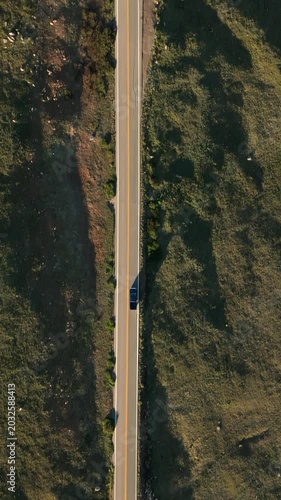 Vertical Screen: Beartooth Highway in Montana USA as a lone car travels along winding mountain road. Drone captures the golden hour light casting long shadows across rocky terrain and green meadows.