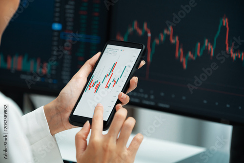 Schilderij op canvas Cropped image in businesswoman using smartphone in profitable of exchange stock market graph comparing with pc screens at modern office